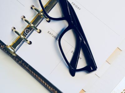 An open paper planner with reading glasses resting on the page