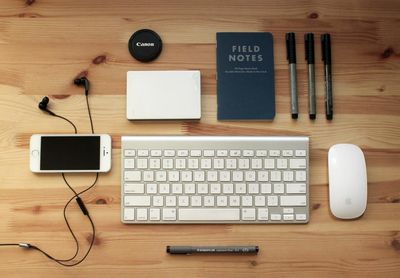 A desk flat lay with a keyboard, a phone, a notebook and earphones